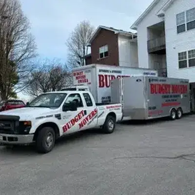Budget Movers truck and trailer parked beside a multi-unit apartment building